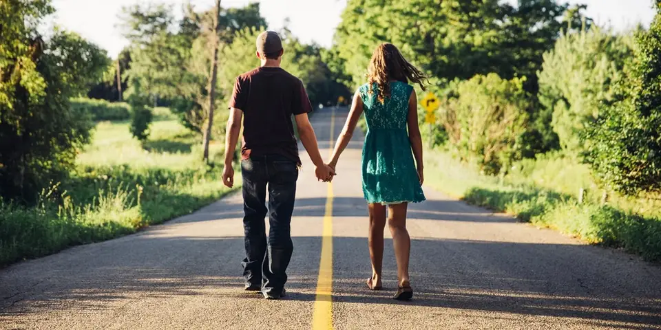 Un couple marche main dans la main sur une route de campagne au soleil