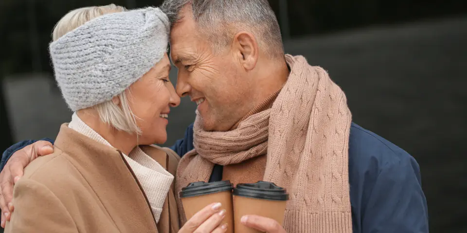 Un couple de seniors se sourit, front contre front, un café à la main