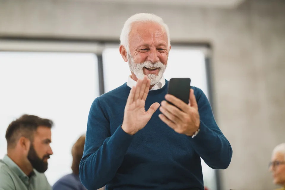 Un homme fait un signe de la main à son interlocuteur pendant un appel vidéo sur son téléphone