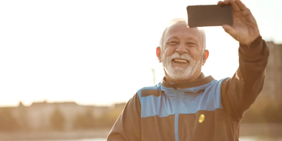 Un homme souriant prend un selfie en extérieur avec son smartphone