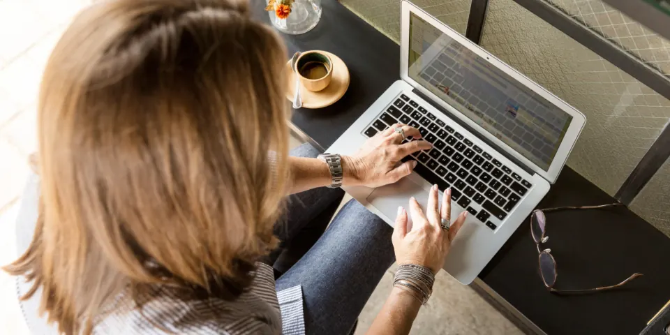 Une femme consulte un site sur son ordinateur portable, vue de dessus, une tasse de café à côté