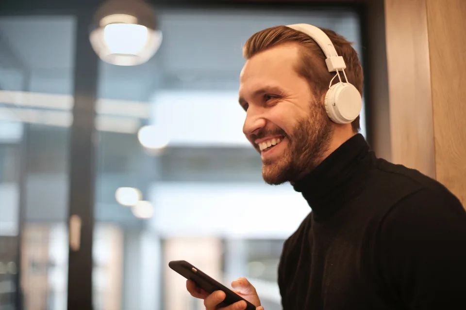 Un homme avec un casque sur les oreilles sourit à son téléphone