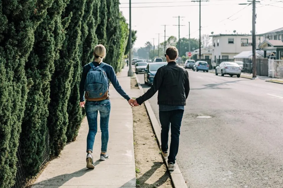 Un couple marche main dans la main sur un trottoir, de dos
