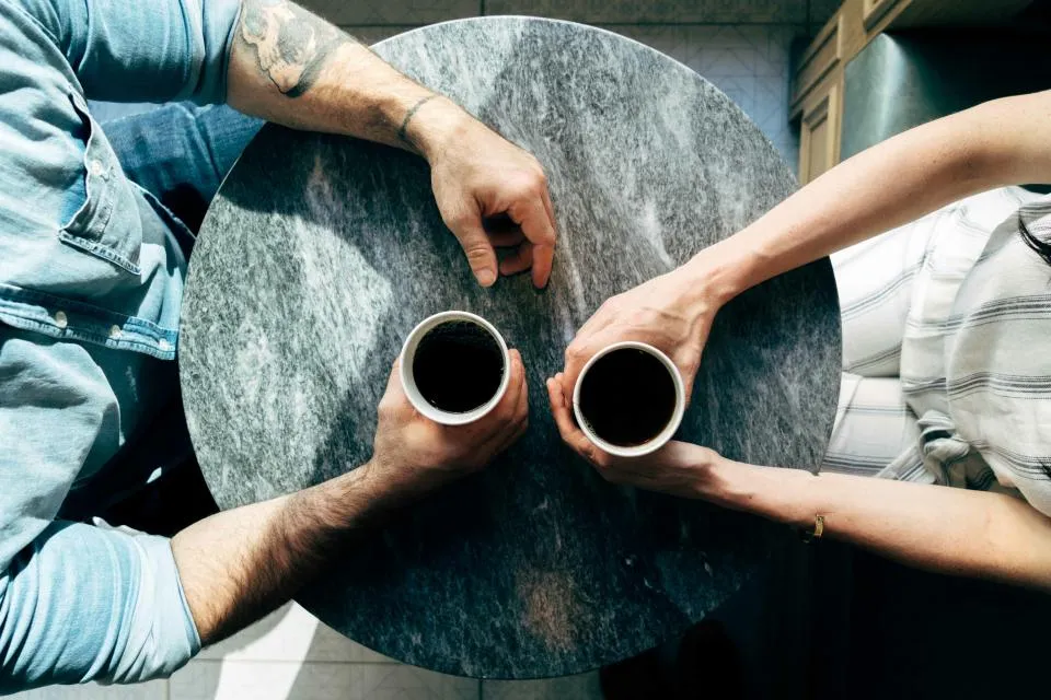 Vue de dessus de deux personnes attablées face à face, chacune tenant une tasse de café
