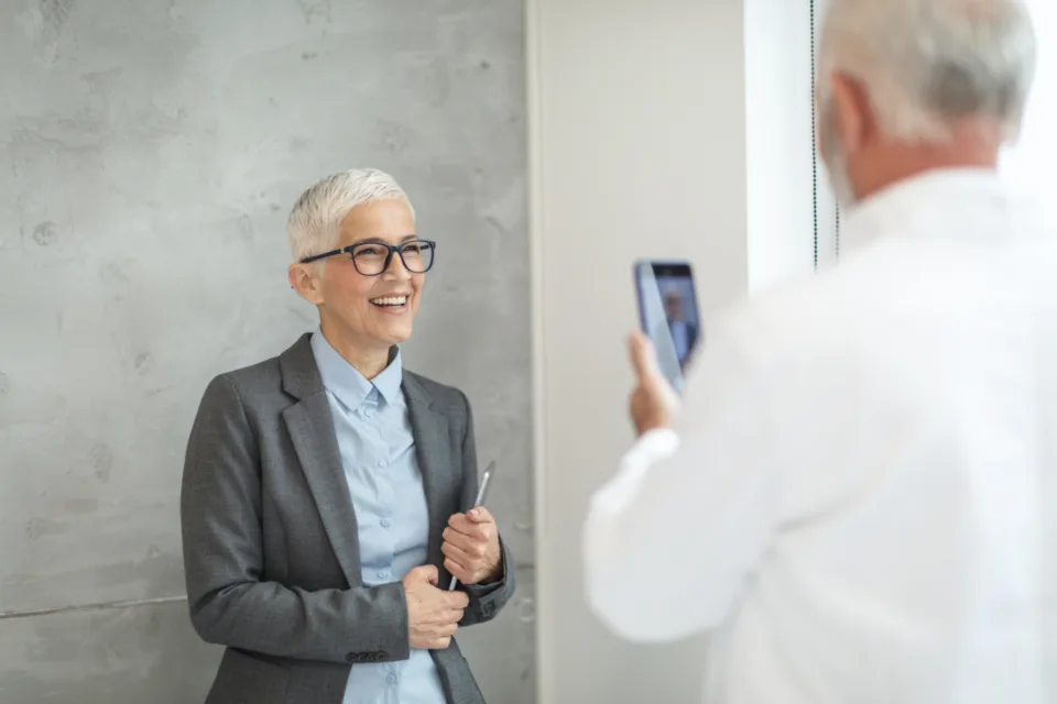 Une femme souriante se fait prendre en photo avec un smartphone